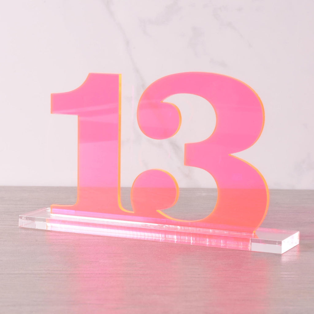 Modern neon pink acrylic table number “13” on a clear base, stylish wedding and party reception centerpiece decoration.