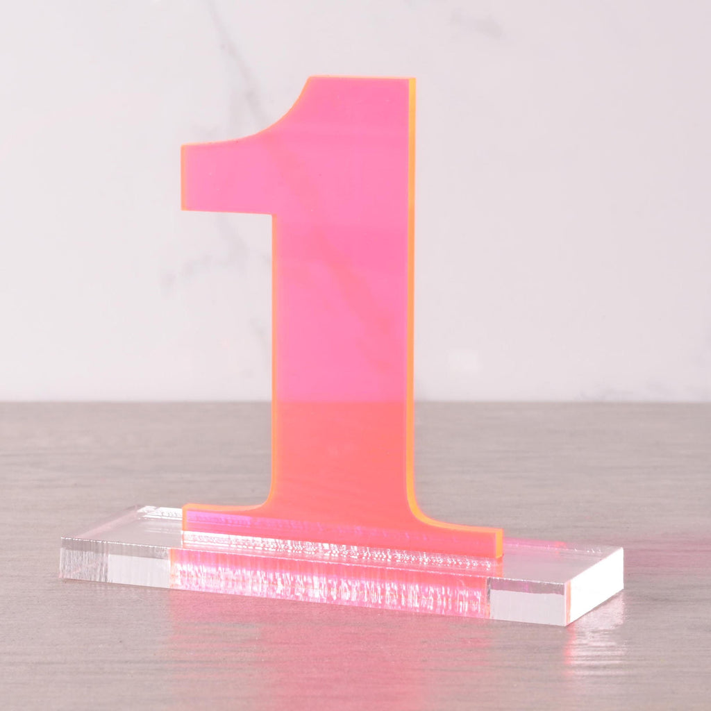 Modern neon pink acrylic table number “1” on clear base, stylish wedding and reception centerpiece decoration.