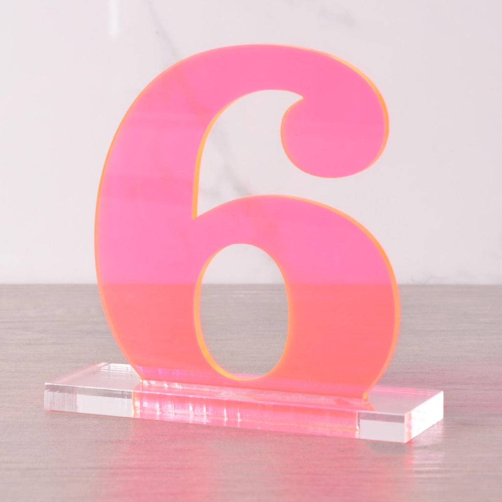 Bright neon pink acrylic table number “6” on a clear base, modern wedding and reception centerpiece decoration.