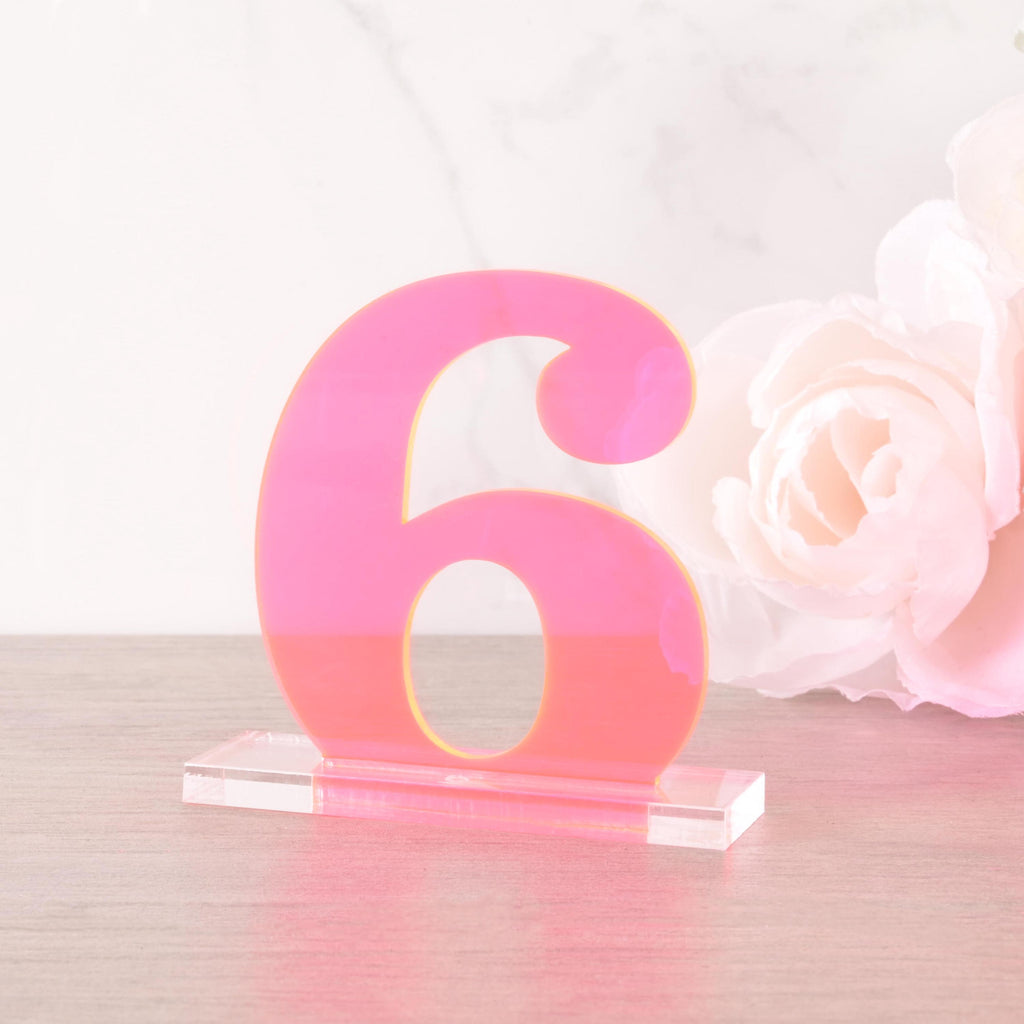 Neon pink acrylic table number “6” on a clear base, styled with a soft white rose flower, ideal for wedding and event centerpieces.