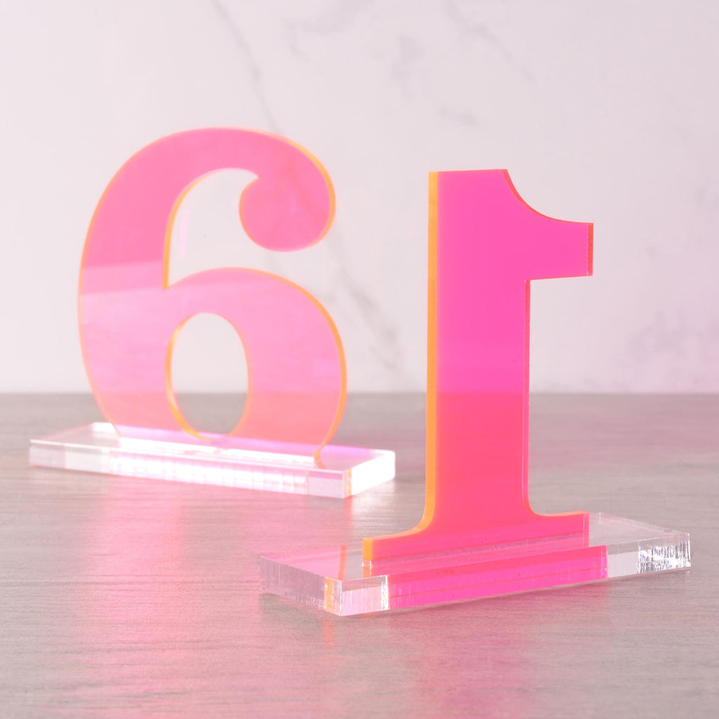 Bright neon pink acrylic table numbers “1” and “6” displayed on clear bases, modern wedding reception centerpiece décor.