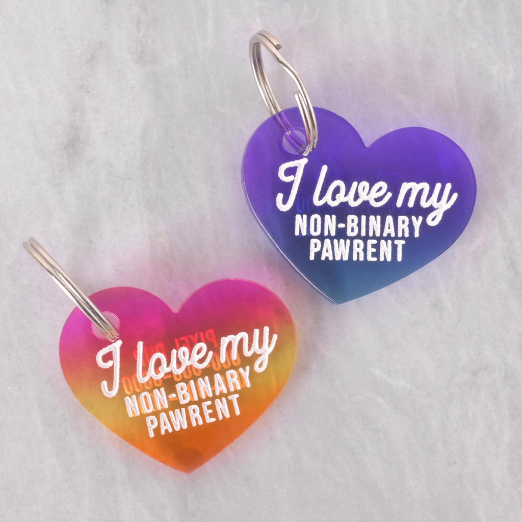 Heart-shaped acrylic pet ID tags in rainbow and purple gradients with the text “I love my non-binary pawrent.”