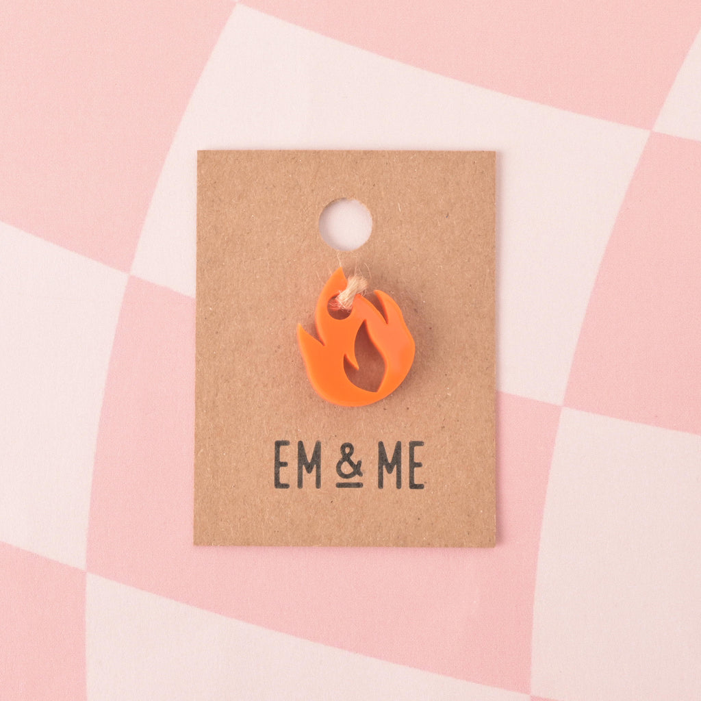 Opaque orange flame-shaped mini charm packaged on a brown kraft paper card on pink checked background.