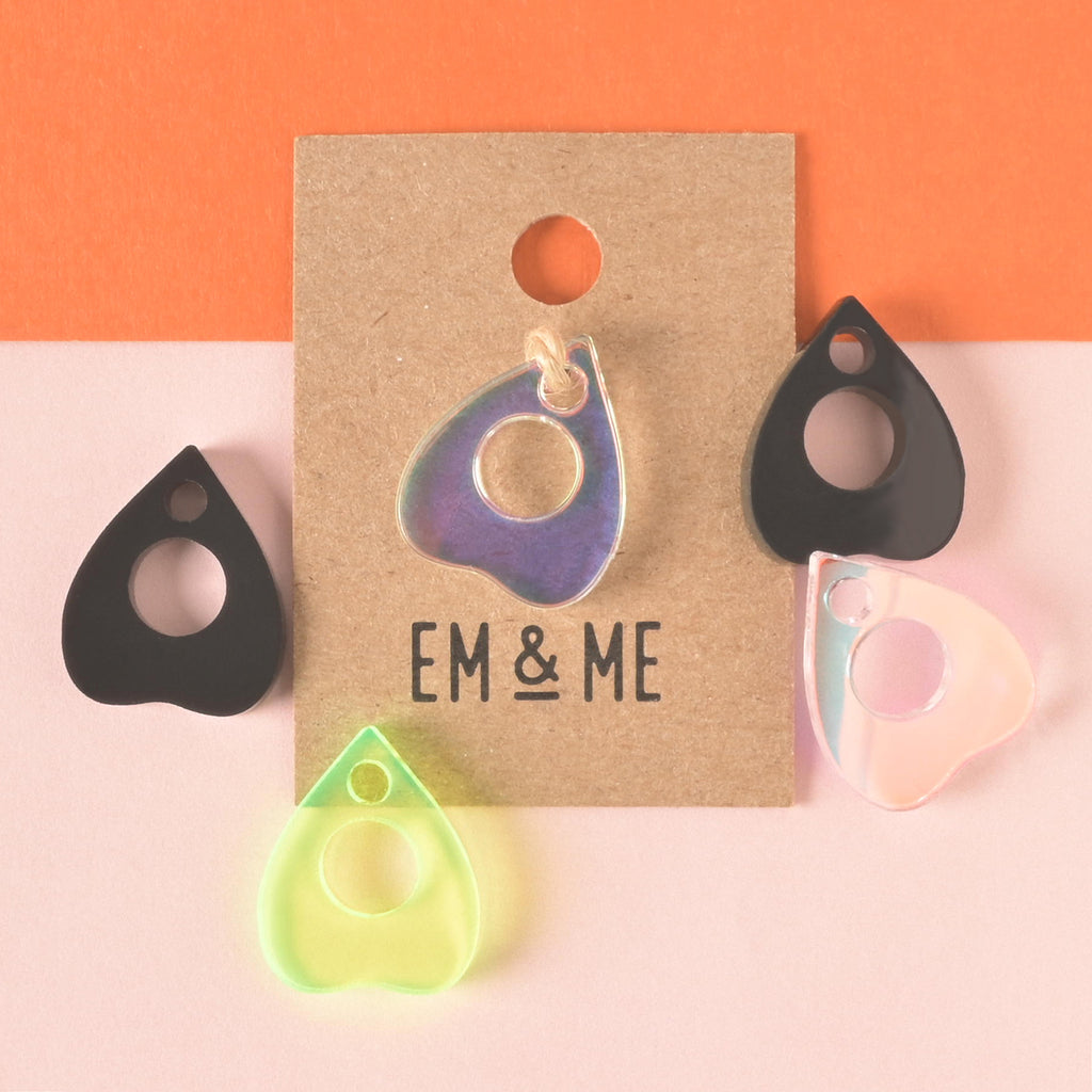 Packaged iridescent ouija mini charm with planchet-shaped charms in fluorescent green, black and iridescent acrylic around it.