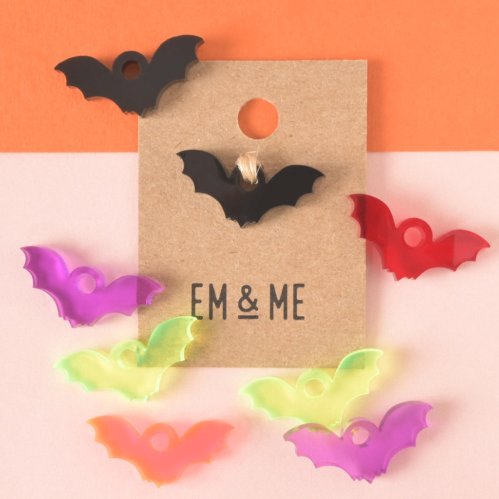 packaged black bat-shaped mini charm on brown kraft paper card surrounded by purple, fluorescent green, red, fluorescent pink and black bat charms
