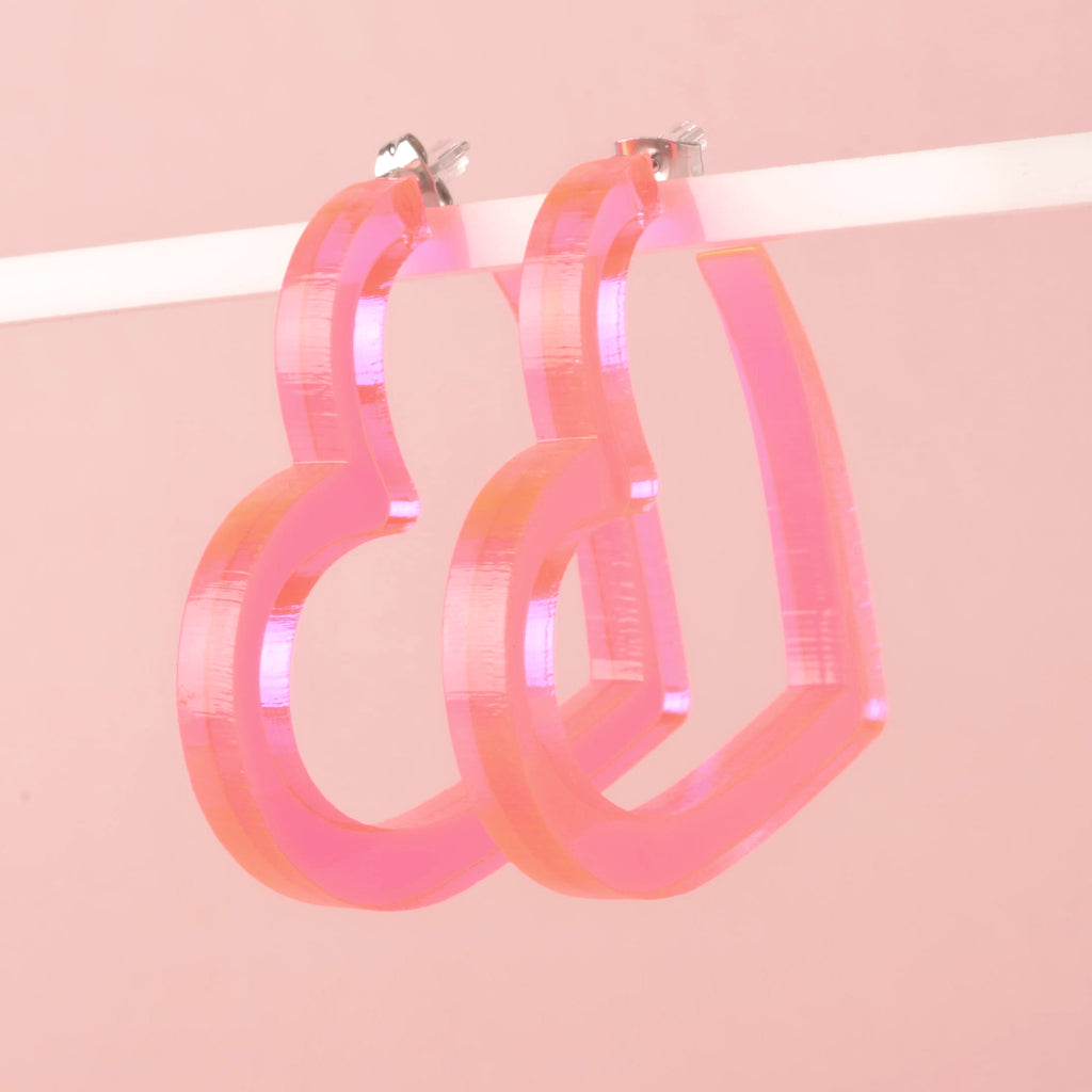 Pair of Fluorescent pink heart-shaped large hoop earrings hanging on solid pink background