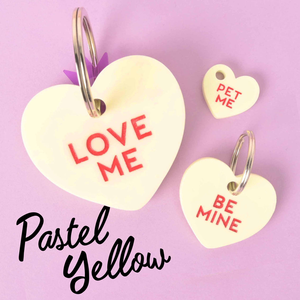 Pastel yellow Conversation Heart pet tags: large “Love Me” Clifford size, regular “Be Mine,” and mini “Pet Me” ID tag on lavender background. Butter Yellow