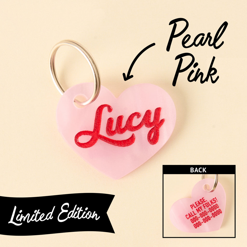 Limited edition pearl pink heart-shaped pet ID tag with engraved name Lucy in red on front and contact info on back, silver keyring attached.