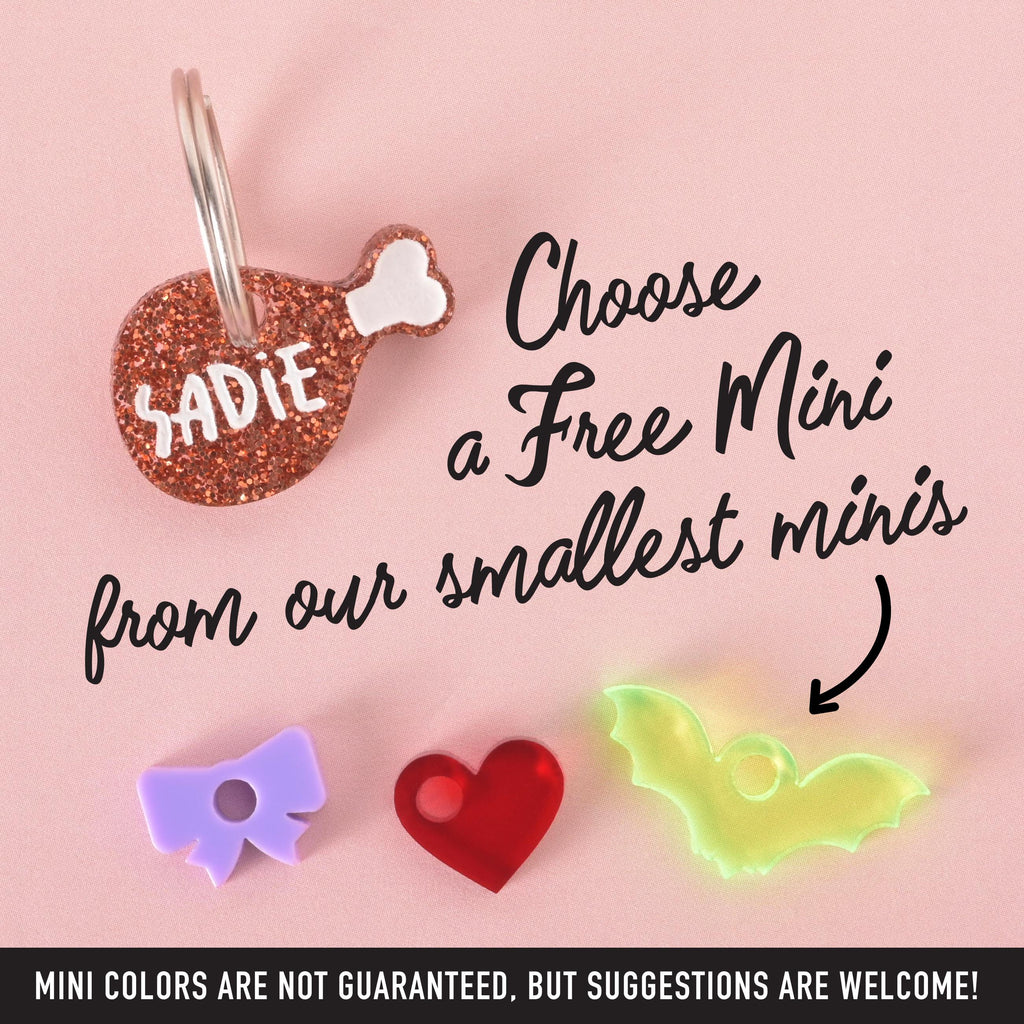Glitter drumstick-shaped custom pet tag with the name “Sadie,” shown with three colorful free mini charms (purple bow, red heart, neon green bat) on a pink background with text overlay offering a free mini add-on.