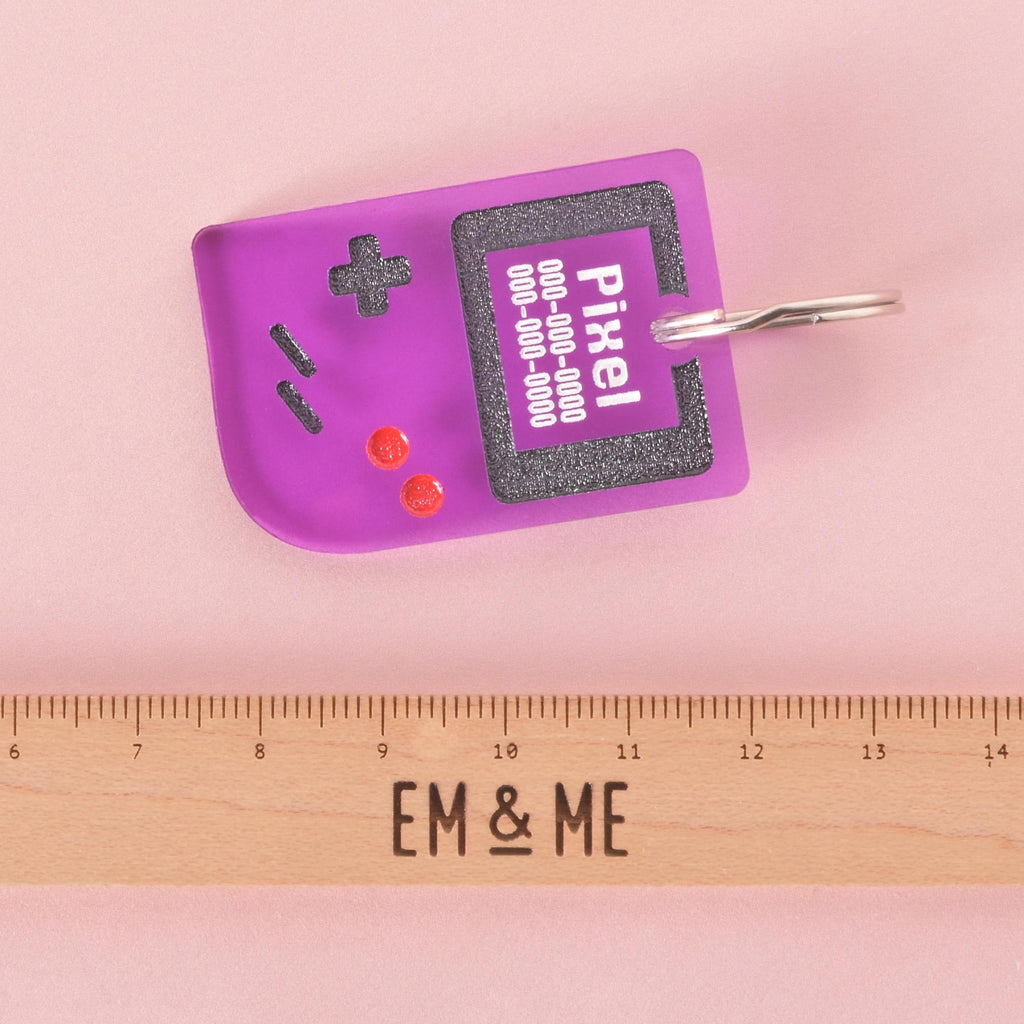 Purple retro game console pet ID tag with engraved pet name and phone number, shown with ruler for size reference, fun customizable dog and cat collar accessory.