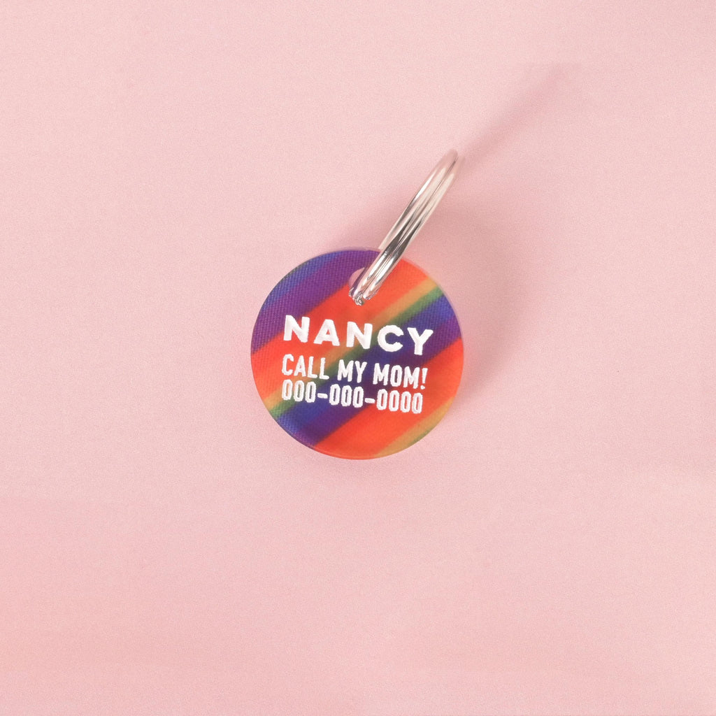 Round rainbow-striped pet ID tag with custom name and phone number, shown with text “Nancy, Call My Mom” for dogs and cats.
