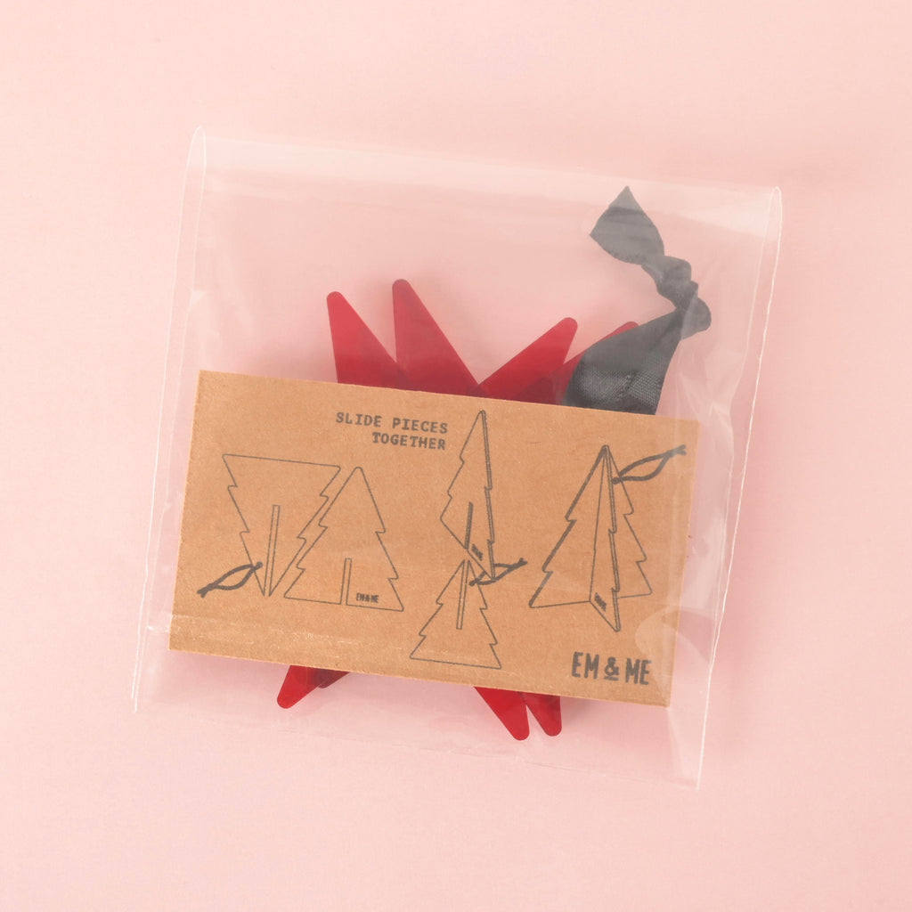 Flat-pack red acrylic Christmas tree ornament in clear packaging with illustrated instructions, holiday decor by EM & ME.