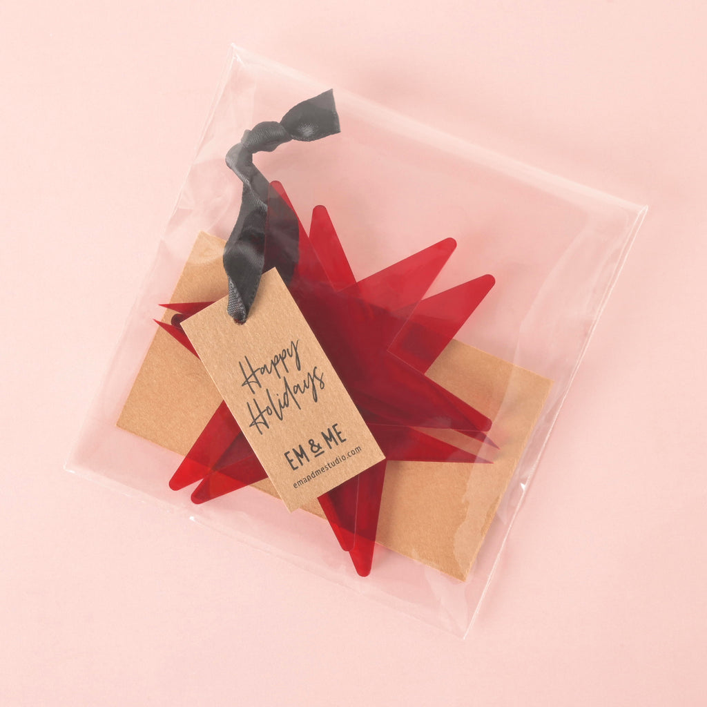 Red acrylic star ornament with black ribbon, packaged in clear bag with kraft Happy Holidays tag, festive decor by EM & ME.