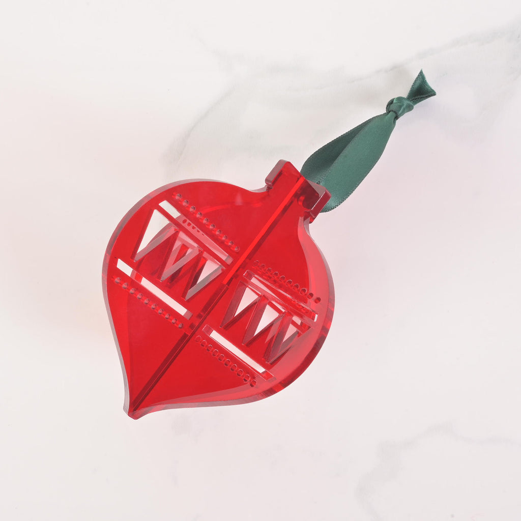 A red flat-pack Christmas tree ornament shaped like a classic glass icicle ornament. The ornament is assembled and has a dark black ribbon tied to the top for hanging. The item is displayed on a white marble surface.