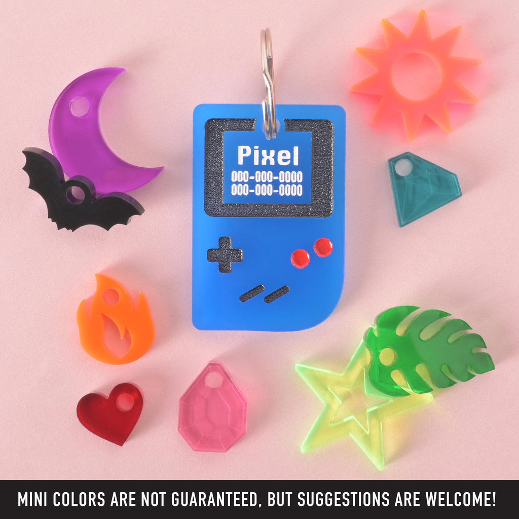 Blue retro game console pet ID tag with custom engraving, shown with colorful mini charm options including star, moon, sun, heart, bat, flame, leaf, and gem, fun design for dogs and cats.