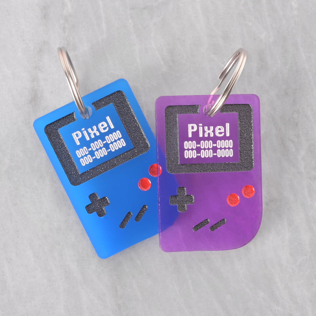 Set of two retro game console pet ID tags in blue and purple, engraved with pet name and phone number, fun customizable dog and cat collar accessories.