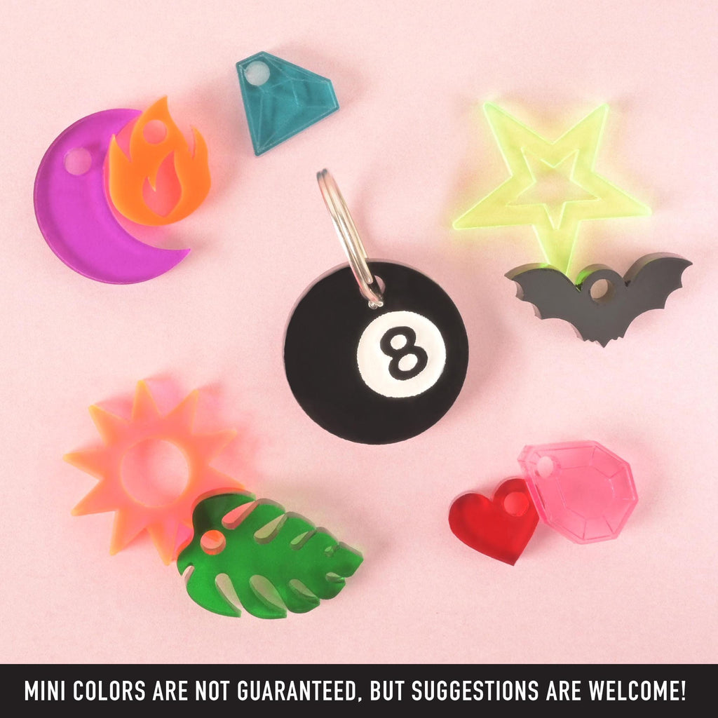Black 8-ball acrylic pet ID tag with a silver keyring, surrounded by colorful mini acrylic charms including a star, moon, heart, gem, and flame.
