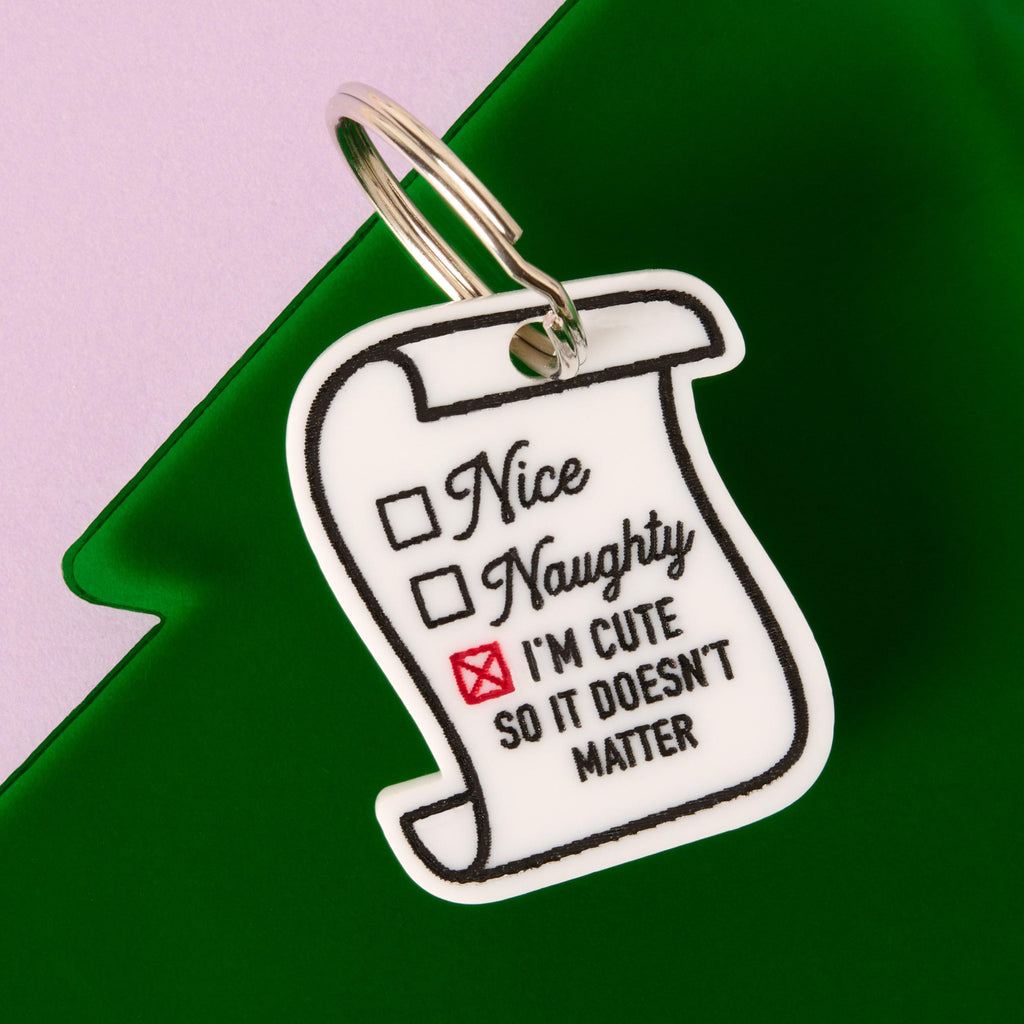 Santa’s Naughty or Nice Pet Tag – “I’m Cute So It Doesn’t Matter” Personalized Dog Tag, Funny Christmas Pet ID Tag Gift
A white scroll-shaped pet tag featuring a naughty or nice checklist. The tag is marked with a red 'X' next to the text "I'M CUTE SO IT DOESN'T MATTER." The tag is attached to a silver ring and is resting on a green Christmas tree shape against a purple and pink background.