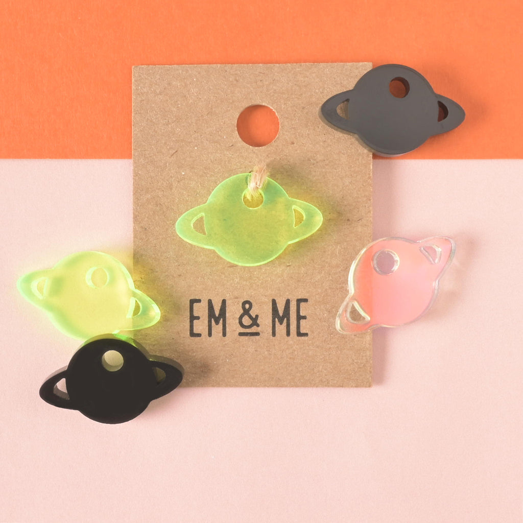 Fluorescent green Saturn-shaped mini charm packaged on brown kraft paper surrounded by more Saturn mini charms 