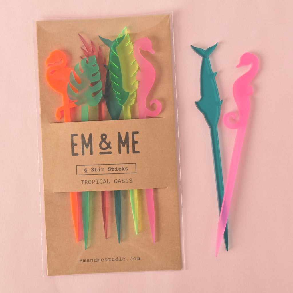 A packaged set of six tropical cocktail stirrers, including a fluorescent pink flamingo, a green monstera leaf, a fluorescent green palm frond, a teal dolphin, a pink seahorse and a transparent pink palm frond