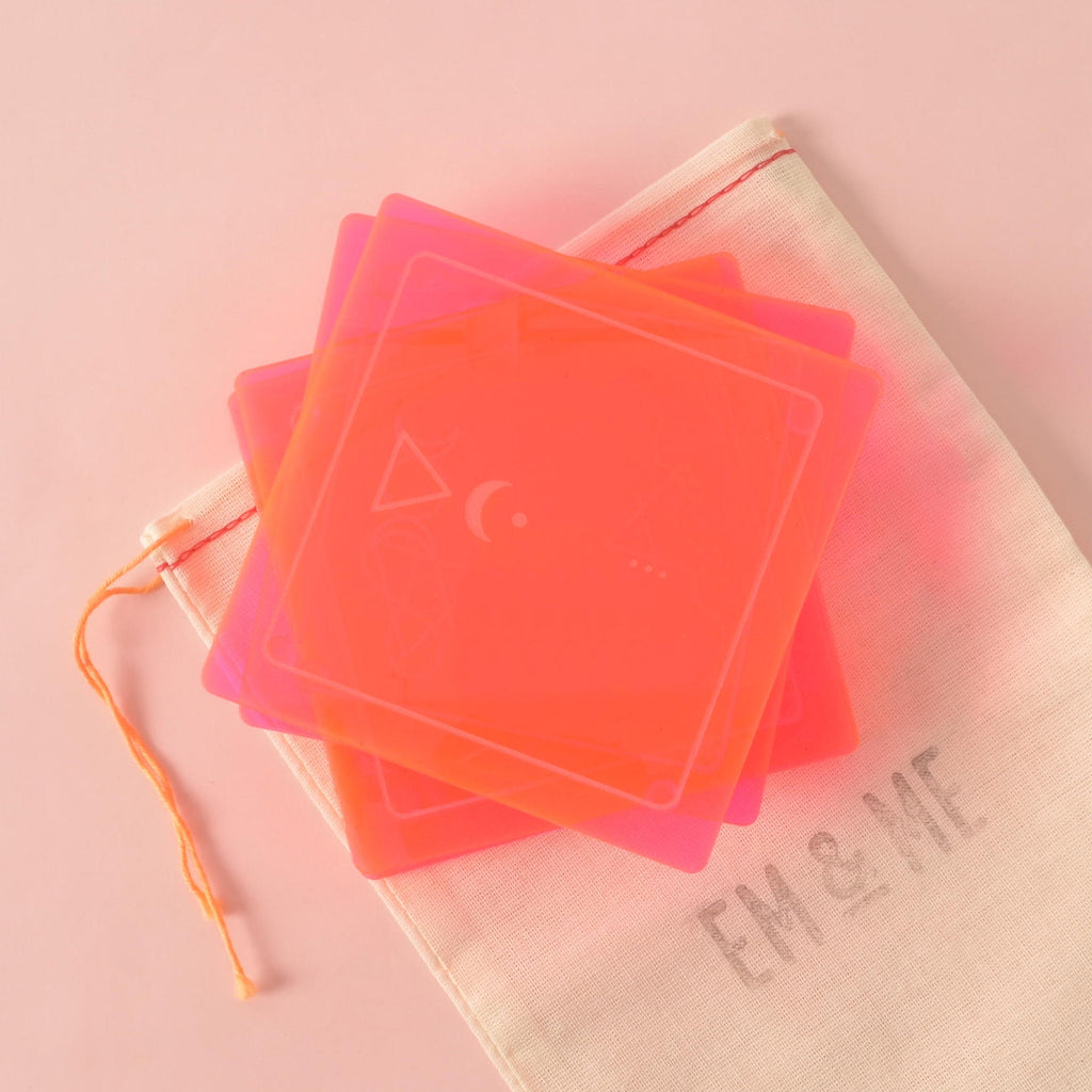 A set of three square-shaped, translucent neon coasters in pink and orange, stacked on a beige pouch. Each coaster has a unique etched design, and the pouch has the "EM & ME" logo. The background is a solid pink color.