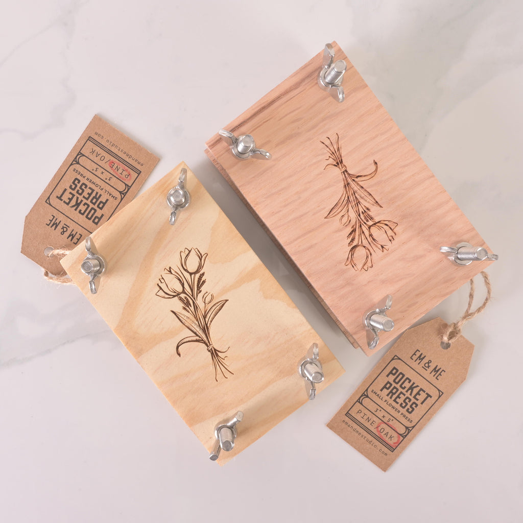 Pair of eco-friendly wooden pocket flower presses with engraved floral artwork and metal wingnuts, ideal for pressing flowers while traveling.