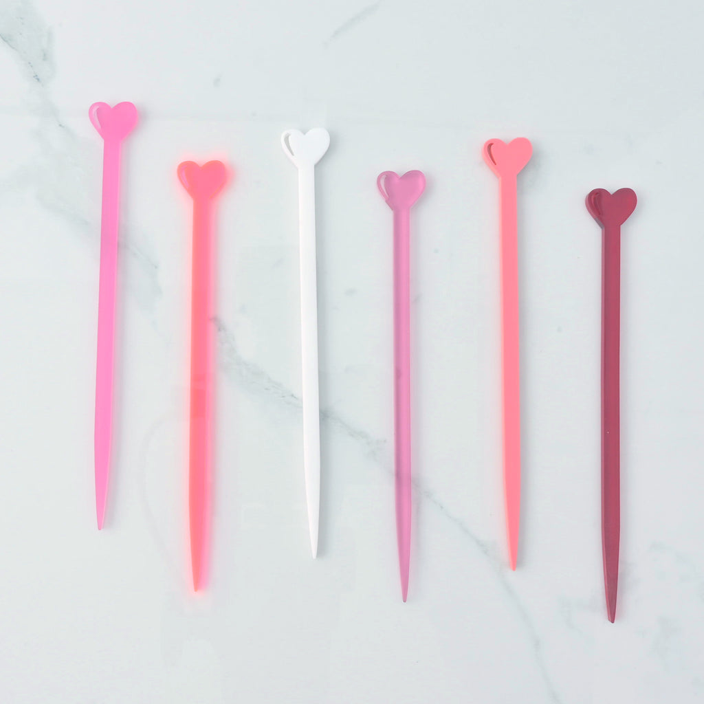 Collection of small heart shaped cocktail stirrers in various shades of pink, red and white on a marble background