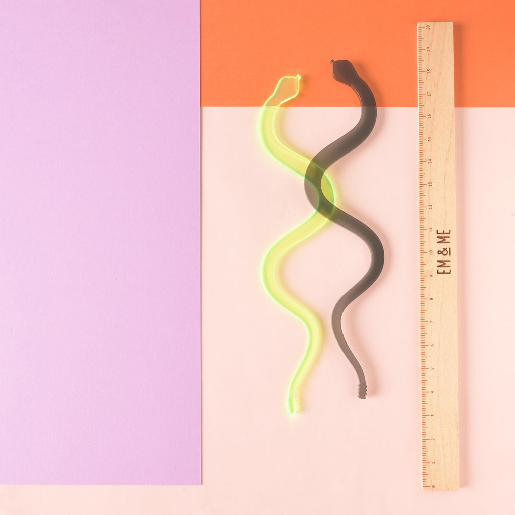 fluorescent green and transparent grey snake-shaped stir sticks next to wooden ruler that reads "EM & ME" on color blocked background