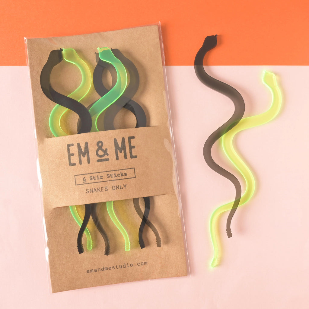 set of 6 snake-shaped cocktail stir sticks packaged on brown kraft paper on color blocked background with two snakes off to the side.