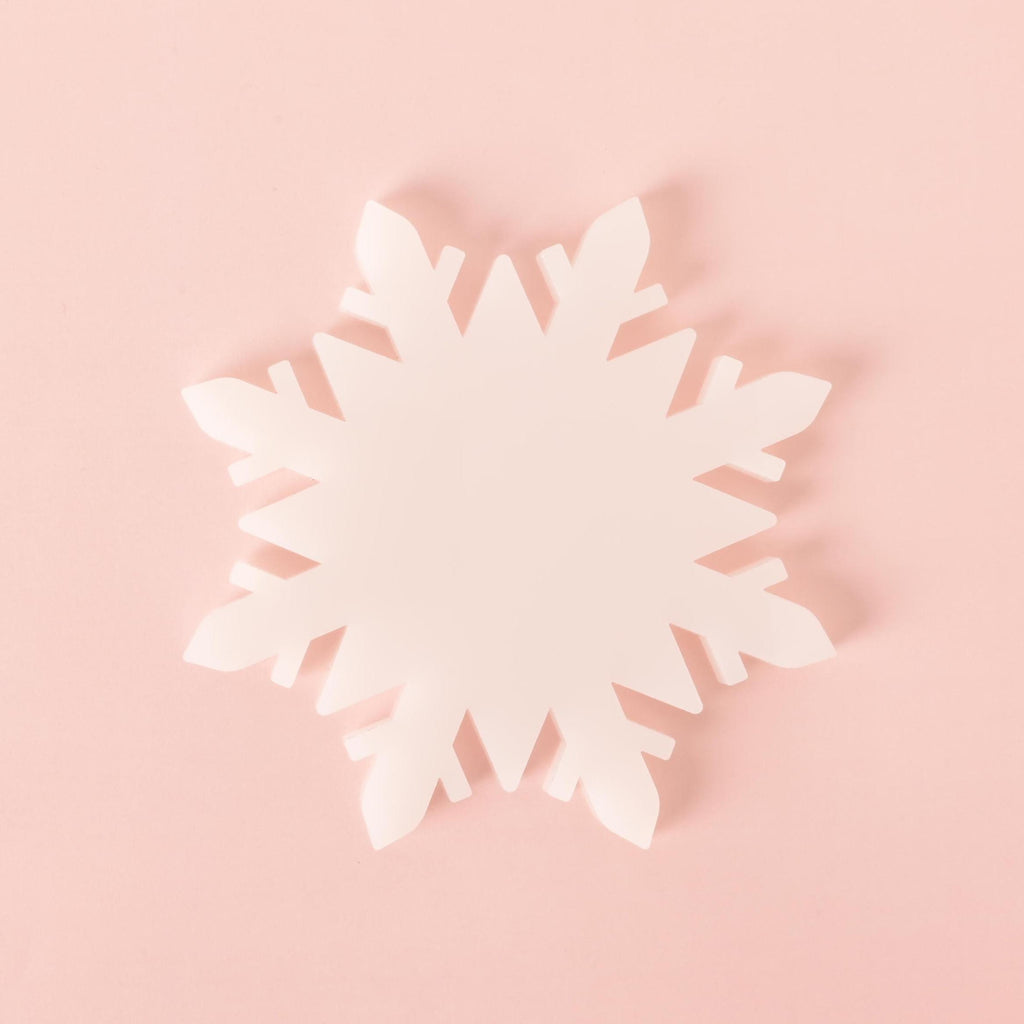 White acrylic snowflake-shaped coaster on a pastel pink background, ideal for protecting tables during winter and holiday gatherings.