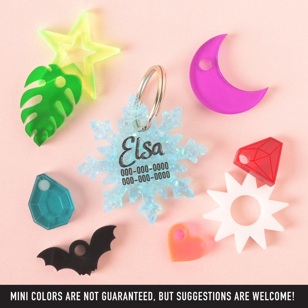 Personalized snowflake pet ID tag engraved with the name Elsa and phone number, surrounded by colorful mini acrylic charms in shapes like star, moon, heart, leaf, bat, gem, and flower.