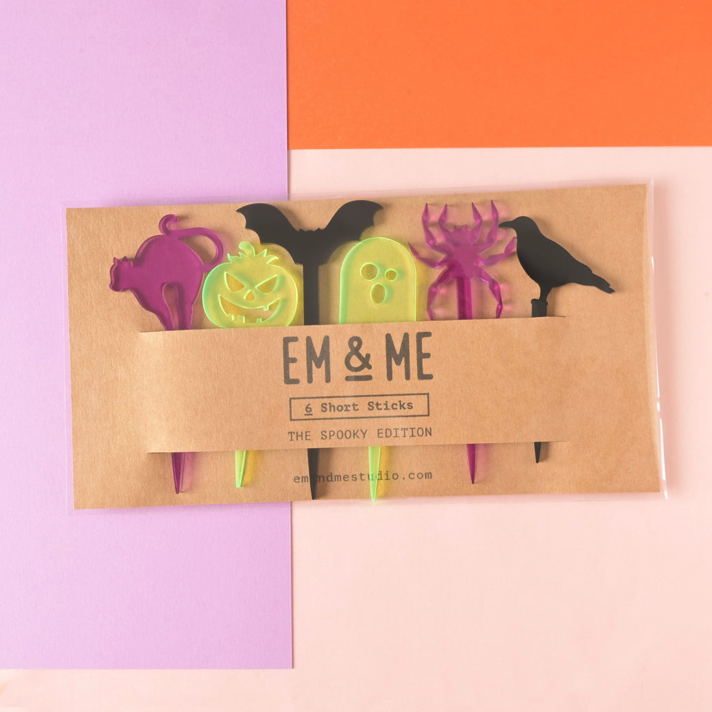collection of 6 halloween themed short food picks packaged on brown kraft paper on color blocked background.