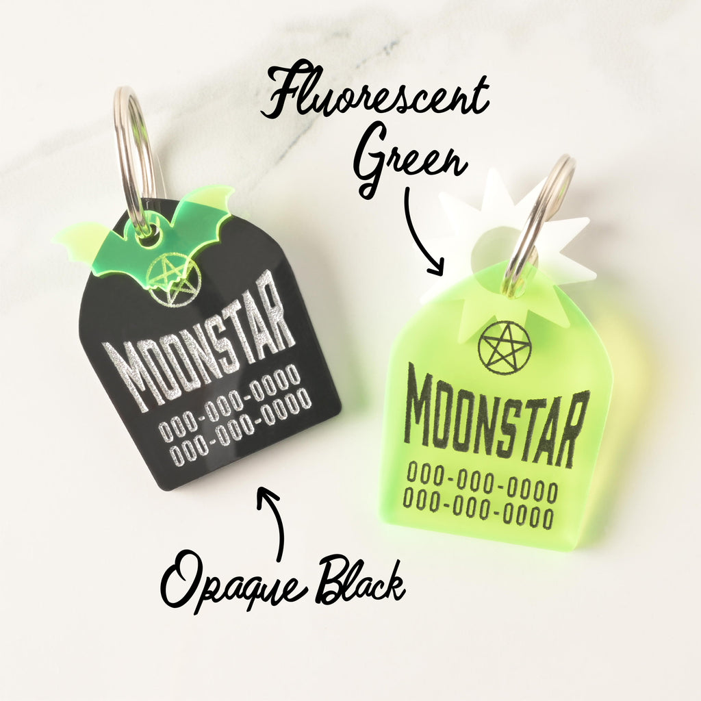 Two tombstone personalized pet tags in opaque black and fluorescent green acrylic. Sun and bat mini charms on solid white background