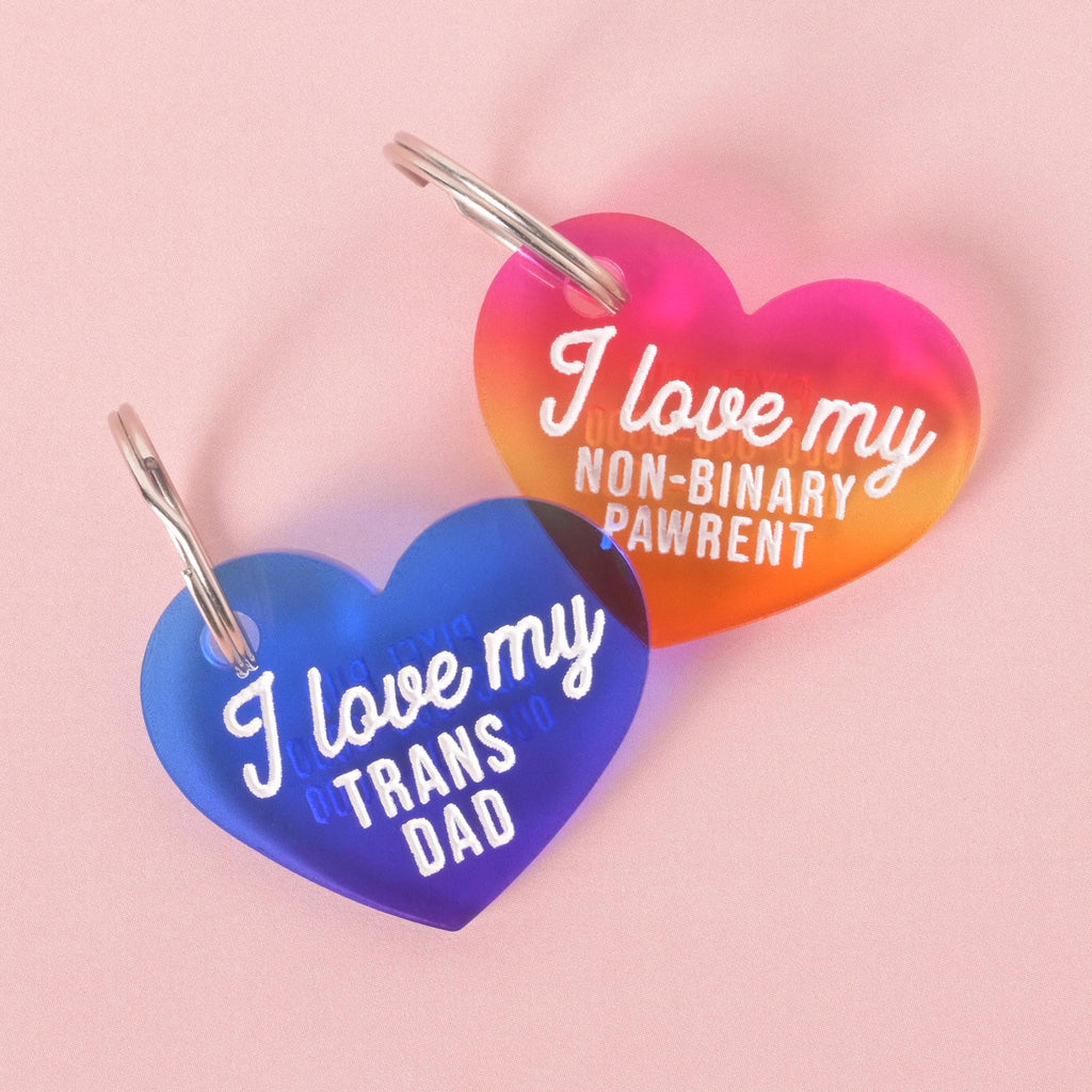 Colorful heart-shaped acrylic pet ID tags with the phrases “I love my trans dad” and “I love my non-binary pawrent.”