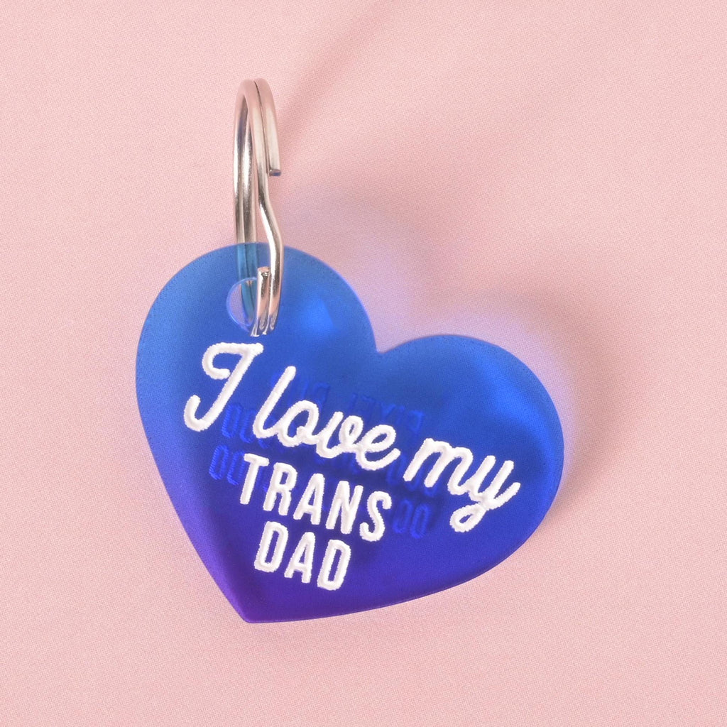 Blue heart-shaped acrylic pet ID tag that reads “I love my trans dad” in white lettering.