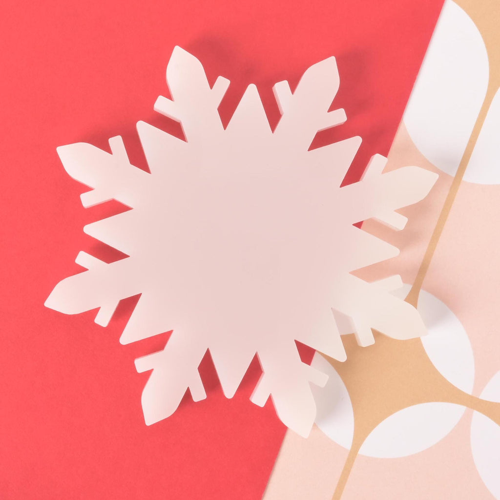 White acrylic snowflake-shaped coaster on a red and patterned background, ideal for winter drinks and Christmas home décor.