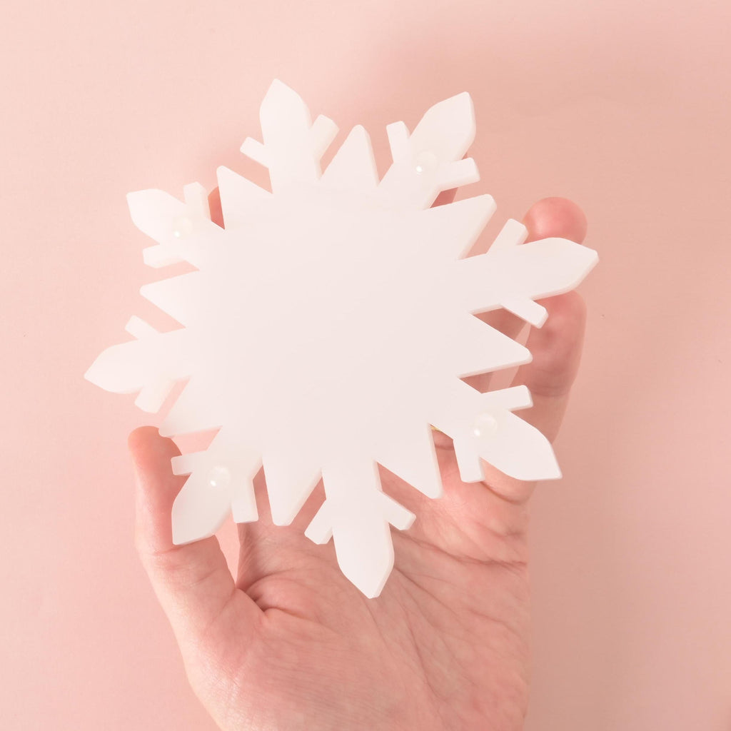 Hand holding a white acrylic snowflake-shaped coaster, perfect for winter drinks and festive holiday table décor.
