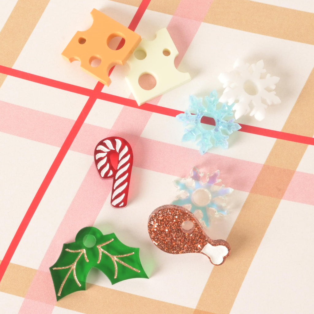 Hosting with food Assorted acrylic holiday mini charms for pet tags, including cheese, snowflakes, candy cane, holly leaves, turkey leg, and more, displayed on a plaid background.