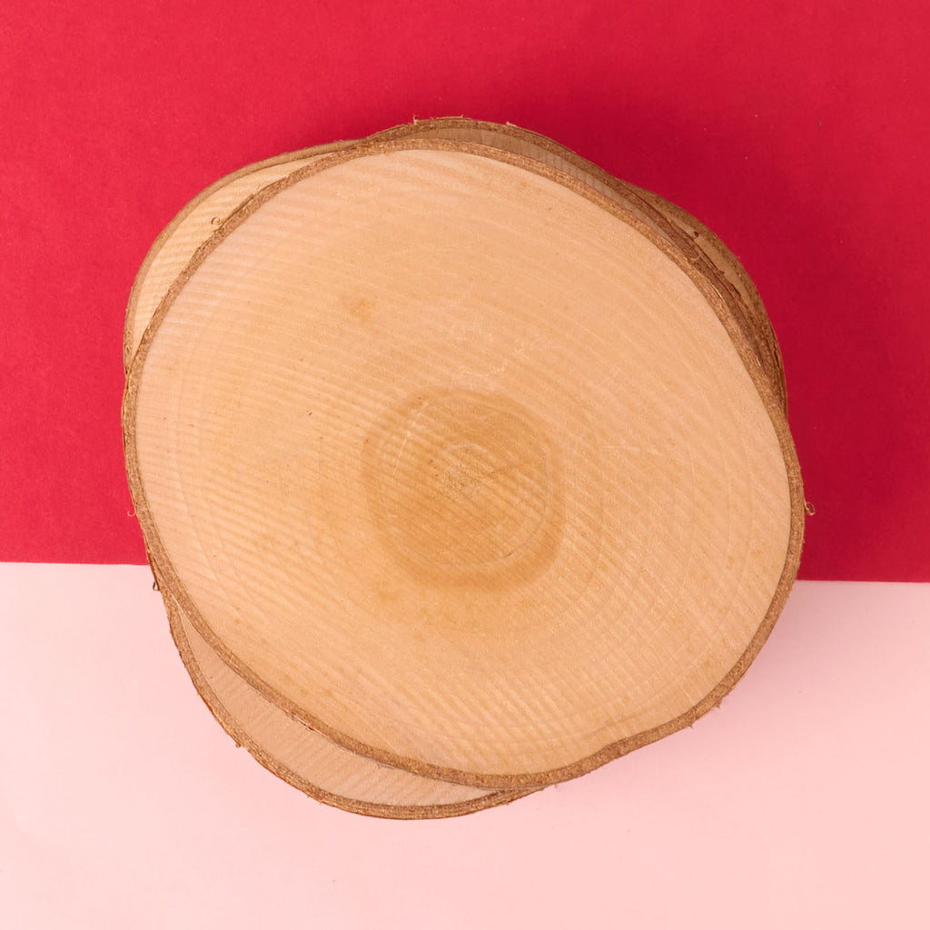 A small stack of circular, natural wood slices with visible growth rings and bark edges. These unfinished wood discs are suitable for use as rustic coasters or craft blanks for pyrogrophy.