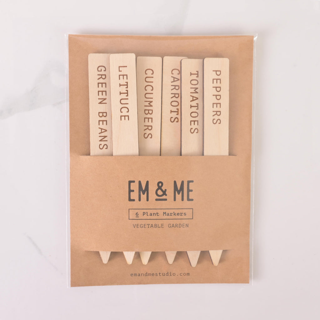 Set of six wooden vegetable garden plant markers labeled Green Beans, Lettuce, Cucumbers, Carrots, Tomatoes, and Peppers, packaged in a kraft paper sleeve branded EM & ME.