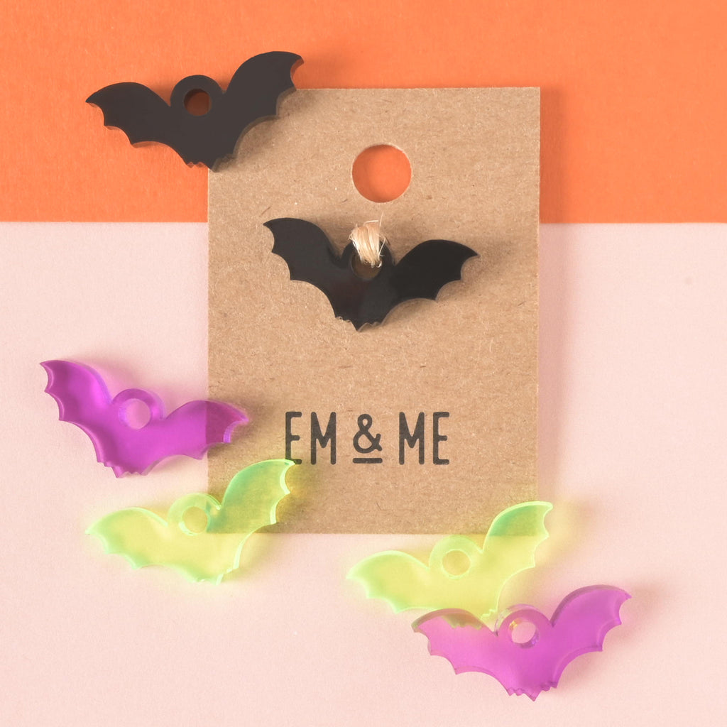 black bat-shaped mini charm packaged on brown kraft paper card surrounded by other bat minis in purple, black and fluorescent green on color blocked background