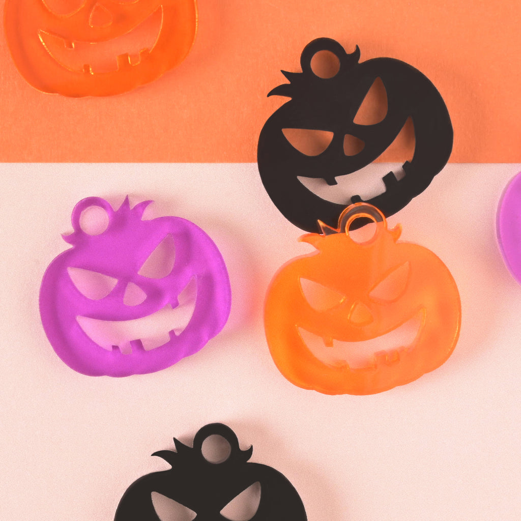 close up of purple, orange and black jack-o-lantern shaped seasonal mini charms on color blocked background
