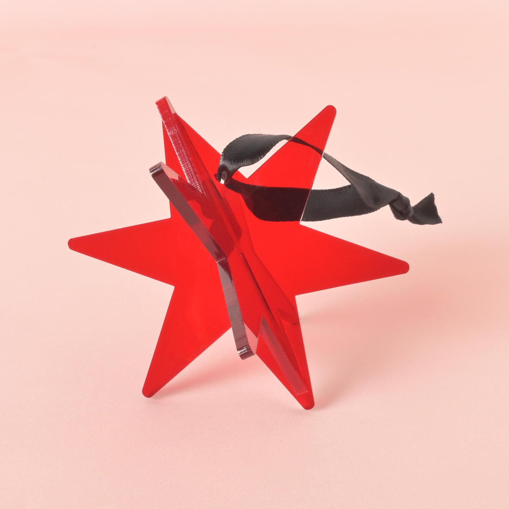 Flat lay of red acrylic star ornament with black ribbon – minimalist Christmas decoration for tree or gift packaging