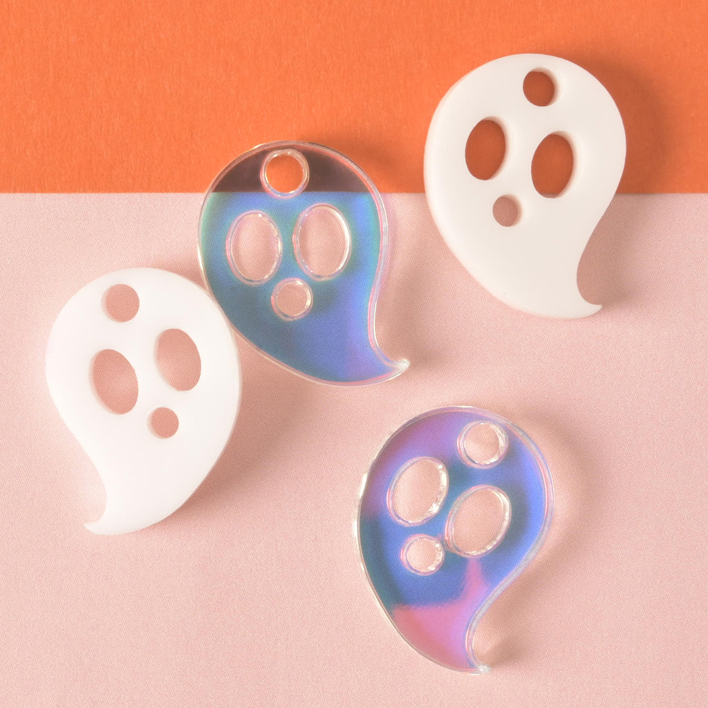 close up of four ghost-shaped mini charms. Two opaque white, two iridescent on color blocked background