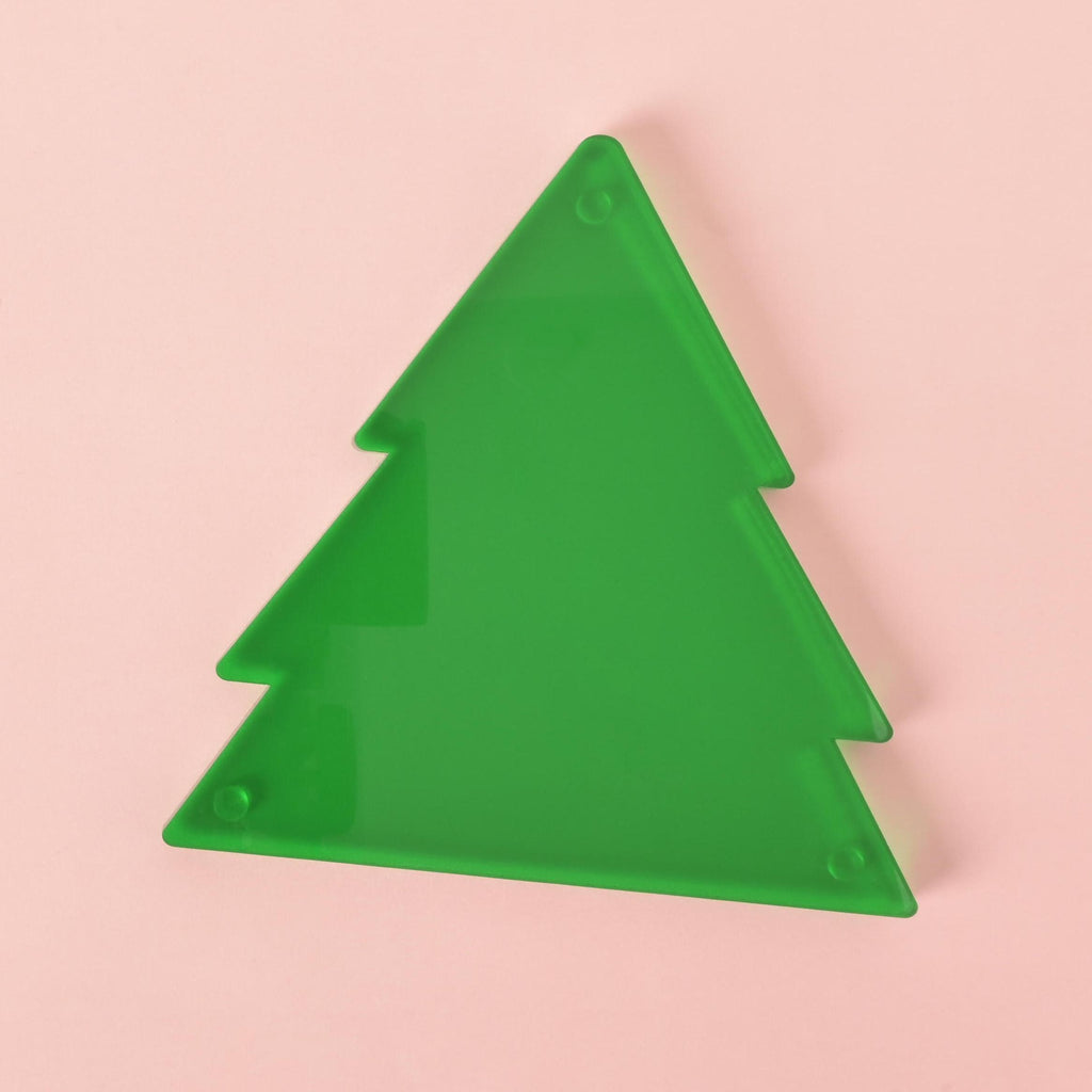 Flat lay of green acrylic Christmas tree ornament on pastel pink background – modern and minimalist holiday decor piece