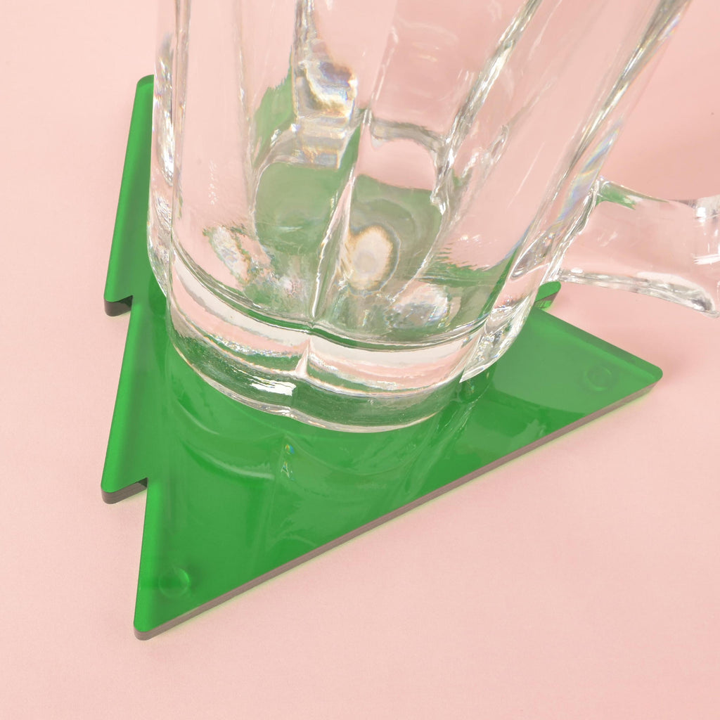 Glass mug resting on a green acrylic Christmas tree-shaped coaster – modern holiday table decor or drinkware accessory