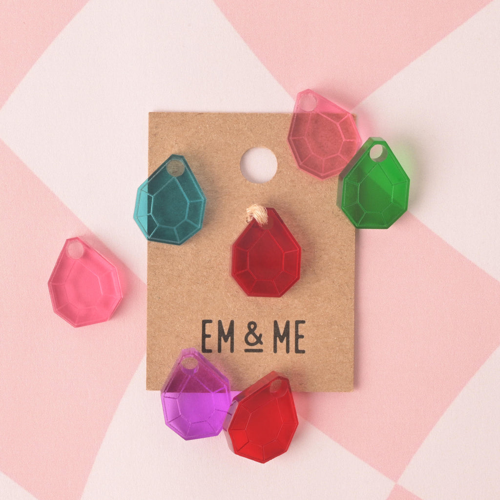 gem-shaped mini charm in red, teal, green, pink, and purple colors packaged on brown kraft paper card on pink checked background.