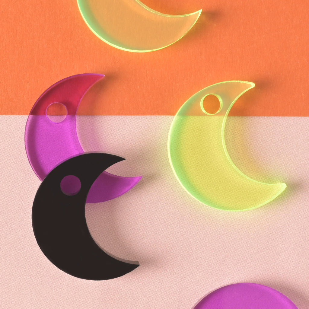 close up of a collection of moon-shaped seasonal mini charms in fluorescent green, purple and black on color blocked background