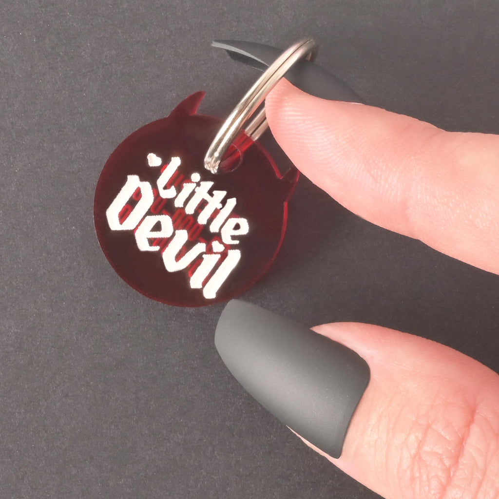 red "little devil" personalized pet tag held by hand with long black finger nails on black background