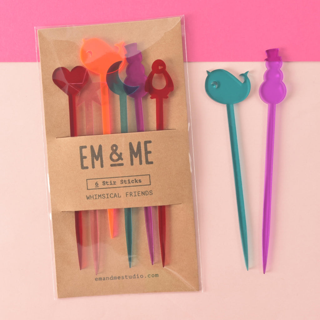 Collection of 6 drink swizzle sticks. heart, star, moon, penguin, snowman and narwhal shapes in red, teal, pink, purple and fluorescent pink acrylic packaged on brown kraft paper